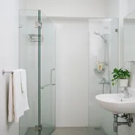 A bathroom with a glass shower screen, white tiles and folded towels